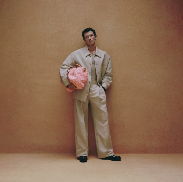 person wearing a lightcolored suit and holding a pink designer backpack against a textured background