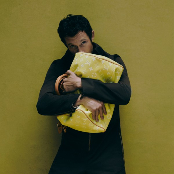 person holding a yellow designer bag against a green background