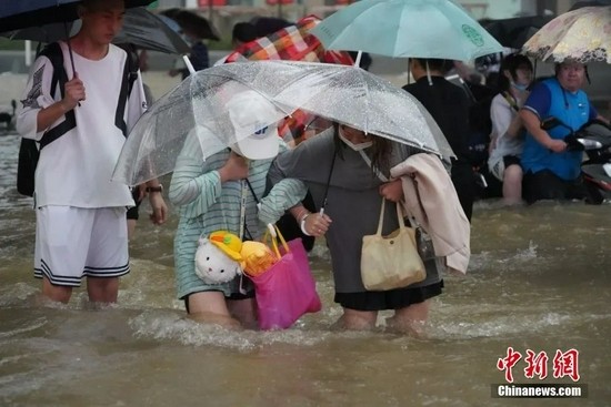 7月20日，河南郑州暴雨成灾。图为市民相互搀扶穿过积水的马路。中新社记者 李超庆 摄