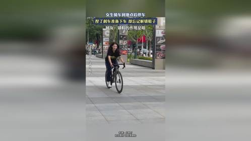女生骑车到地点后停车，捏了刹车准备下车，却忘记解锁鞋子。