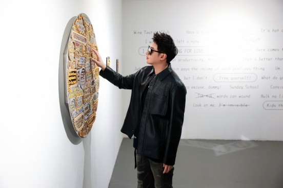 individual interacting with a textured wall art piece that features various colors and patterns