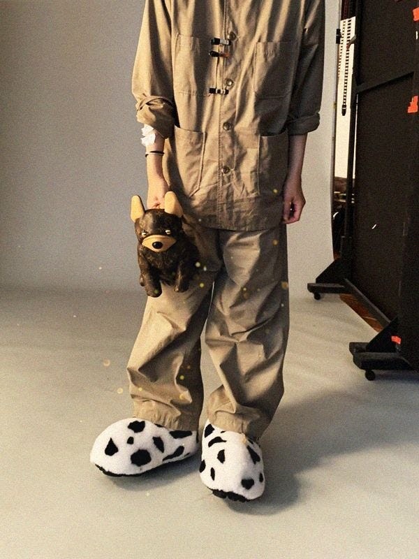 person wearing oversized beige clothing and animalthemed slippers holding a plush toy