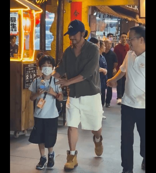 搜狐娱乐讯 近日，网友偶遇吴京带小儿子南宁吃烧烤。吴京穿开领衬衫白色短裤，头戴鸭舌帽扎小辫，随性松弛。