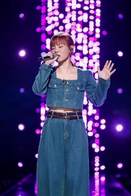 年轻女歌手在舞台上演唱，背景灯光闪烁。