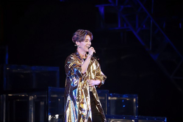 鹿晗明星在舞台上表演，身穿金色亮片外套，微笑着拿着麦克风。