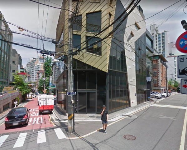 Pledis Entertainment 附近的街道，寧靜的日子，一名身穿黑色休閒服的男士走過交叉路口，背景是現代的城市建築和繁忙的電線分佈。