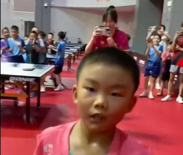 学生在乒乓球馆内拍照，背景有多名学生和一位老师。