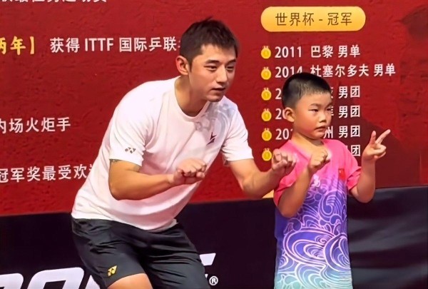 张继科乒乓球运动员与儿童合影，背景显示获奖信息和“世界杯-冠军”标题