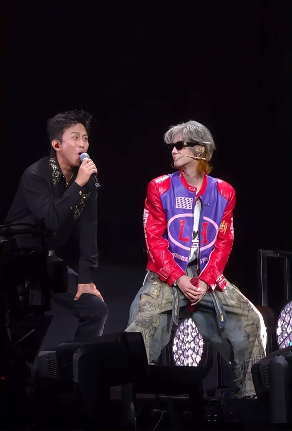 邓超两位艺人在舞台上进行互动表演，一人手持麦克风，另一人戴墨镜穿着亮色夹克。