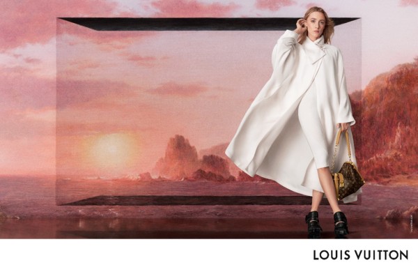 fashion model wearing a white coat and holding a louis vuitton handbag in front of a scenic backdrop