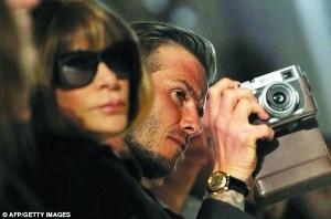 还在台下“兼职”摄影师，拍下妻子的新作，他旁边还坐着大名鼎鼎的“穿Prada的恶魔”、美国版《VOGUE》女主编安娜·温图尔。