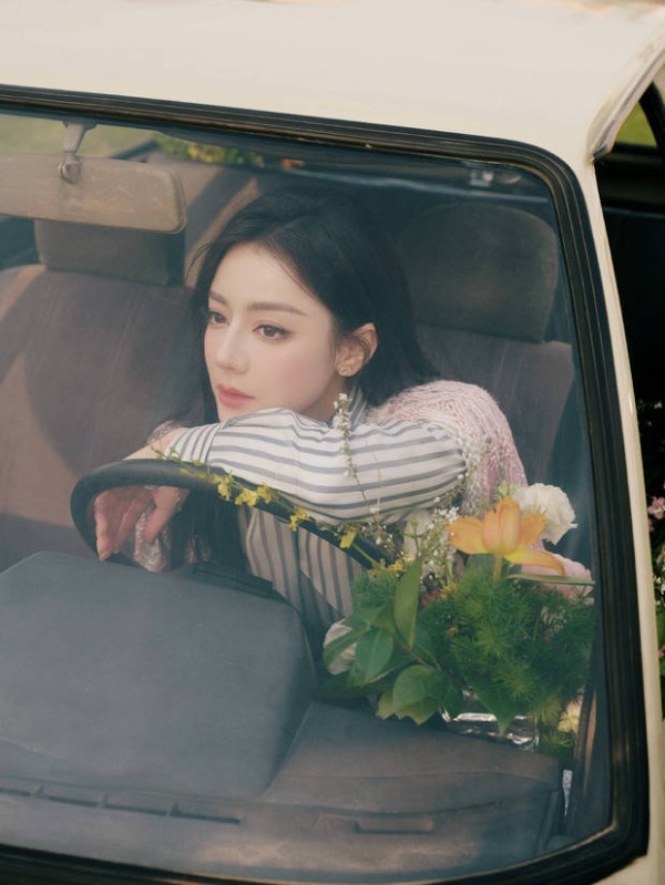 迪丽热巴手搭方向盘,身旁鲜花环绕,眼神温柔,治愈浪漫。