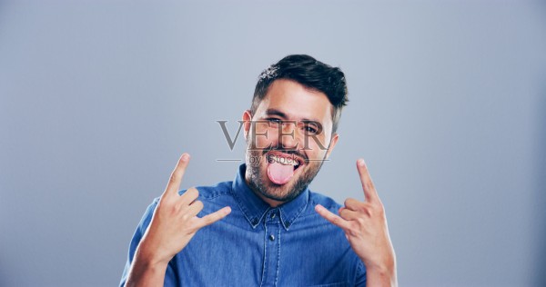 在灰色背景下,空间中快乐或肖像的男人做出摇滚手势,展现狂野的表情。文化,前卫的男性摇滚者和疯狂的人做出魔鬼角手势,搭配有趣的表情符号和朋克标志。照片摄影图片