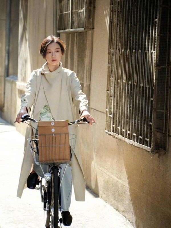 倪妮骑车穿行,风衣造型文艺随性。